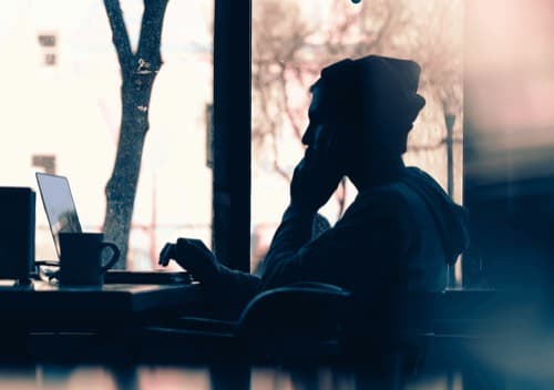 Silhouette of a person working on a laptop by a window